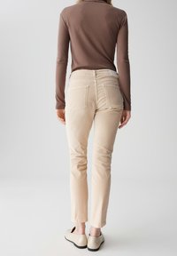 Beige, aansluitende broeken met achterzakken en een slank ontwerp, gecombineerd met een bruin shirt met lange mouwen en lichtgekleurde schoenen.
