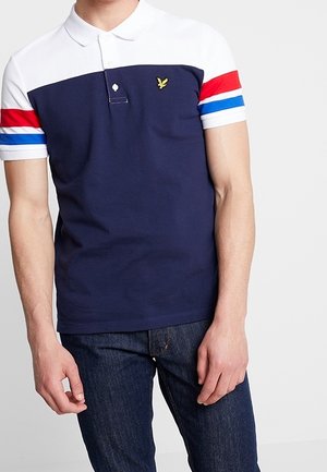 Chemise polo bleu marine avec col blanc et manches courtes, ornée de rayures rouges et bleues. Comprend un petit logo d'aigle jaune sur la poitrine.