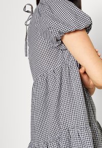 Zwart-witte ruitjesjurk met pofmouwen, een getailleerde taille en een rok met meerdere lagen. Voorzien van een striksluiting aan de achterkant, gemaakt van lichtgewicht stof.