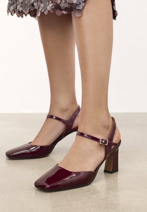 Tacchi slingback in pelle verniciata bordeaux con tacco a blocco, punta affusolata e cinturino alla caviglia regolabile. Finitura liscia e lucida.