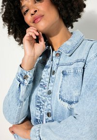 Giacca di jeans light blue con colletto, chiusura a bottoni e dettagli strappati. Presenta grandi tasche e un leggero sbiadimento del tessuto.