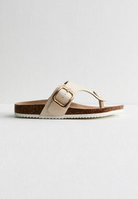 Crème-kleurige sandalen met een teenstuk ontwerp, voorzien van een gouden metalen gesp en een gestructureerde kurken tussenzool, afgewerkt met een witte rubberen outsole.