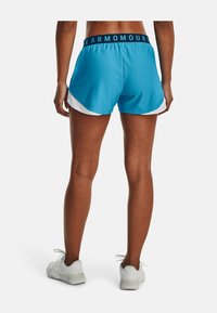 Pantalones cortos deportivos azules con una cintura negra que lleva el texto "ARMOUR". De longitud corta y paneles laterales blancos en contraste. Combinados con zapatos blancos.