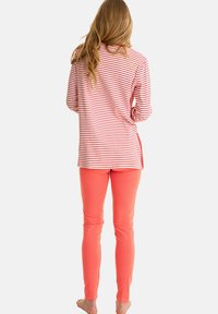 Haut à rayures à manches longues rouge et blanc, associé à un pantalon corail ajusté. Tissu doux, coupe décontractée, fentes sur les côtés du haut.