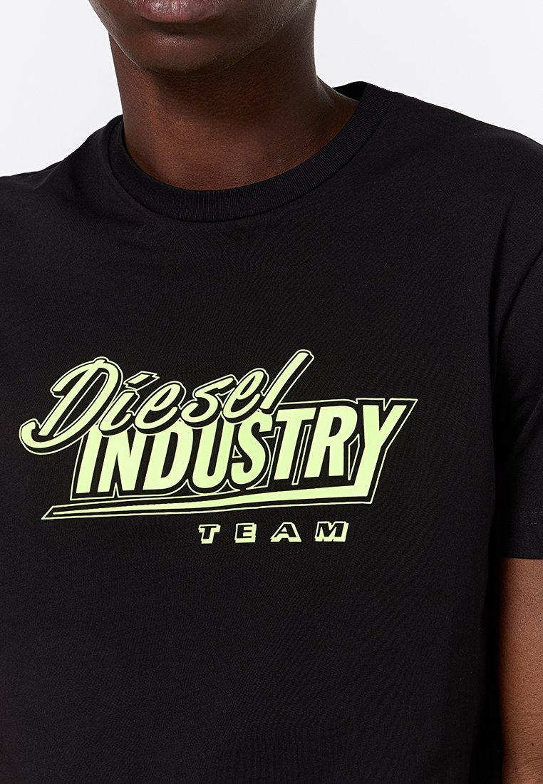 Czarna bawełniana koszulka z okrągłym dekoltem, z wyraźnym żółto-zielonym nadrukiem "Diesel INDUSTRY TEAM". Miękka tekstura.