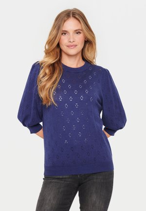 Mørkeblå strikket sweater med pufærmer, der har et geometrisk udskæringsmønster samt ribkant ved nederste kant og ærmer. Glat tekstur, afslappet design.
