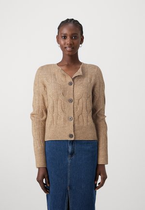 Beige cable-knit cardigan with a V-neck, five brown buttons down the front, and ribbed cuffs. Worn over a blue denim skirt.