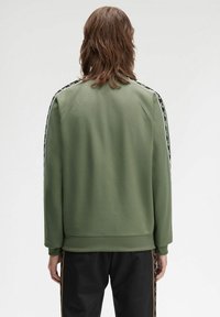Felpa verde con orlo e polsini a costina, caratterizzata da strisce laterali nere con un motivo di logo ripetuto, mostrata da dietro.