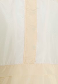 Abito di colore chiaro con una texture liscia; presenta un corpo crema e una cucitura pesca chiara al centro; design e sartoria semplici.