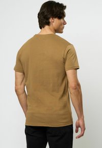 Brun bomull T-skjorte med korte ermer og rund hals. Stoffet ser jevnt ut; passformen er avslappet med en rett kant.