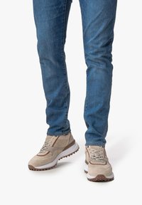Des chaussures de sport beiges et marron avec un dessus en daim texturé et en mesh, une semelle en caoutchouc contrastante et un design à lacets, assorties à un jean bleu.