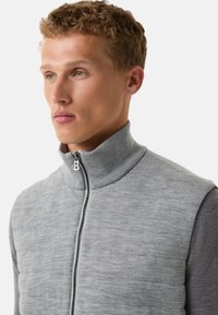 Graue Weste mit hohem Kragen und Reißverschluss, mit einer strukturierten Vorderseite und glatten Ärmeln. Der Stoff hat ein weiches, gestricktes Aussehen.