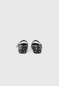 Zwarte schoenen met witte stippen, platte ontwerp, verstelbare enkelband en gladde textuur. Ronde neus met een minimalistische silhouet.