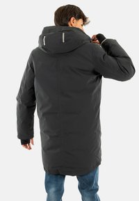Parka negra impermeable con capucha, que presenta acentos reflectantes, mangas largas y un corte recto. El interior está forrado y aislado.