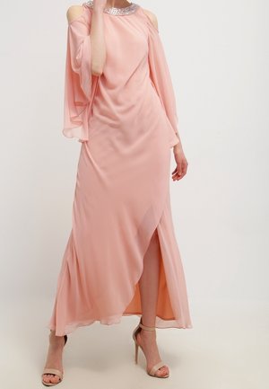 Longue robe rose pâle en tissu fluide, avec des manches tombantes sur les épaules, un col orné de perles, et une fente haute à l'avant.