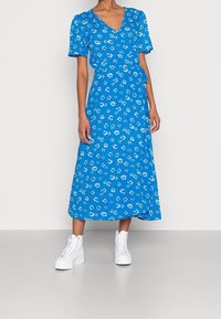 Blommig blå omlottklänning med korta ärmar och midi-längd, gjord av lättviktsmaterial med en mjuk textur. Bärs med vita sneakers.