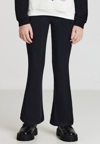 Pantaloni neri a zampa d'elefante realizzati in materiale strutturato, con un motivo a righe. Abbinati a scarpe nere chunky, evidenziano un silhouette contrastante.
