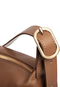Tracolla in pelle marrone con fibbia in metallo dorato. Caratterizzata da una chiusura con zip lungo il lato. Texture liscia con cuciture visibili.