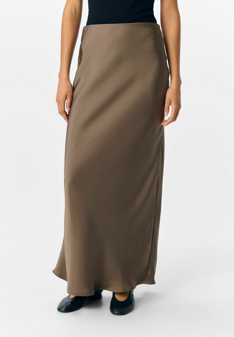 Donna che indossa una gonna in satin marrone, lunga fino alla caviglia, con una leggera svasatura, abbinata a scarpe nere e a un top nero.
