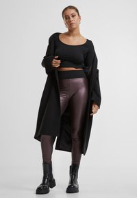 Sort oversize cardigan, tætsiddende sort top og metalliske bordeaux leggings kombineret med chunky sorte støvler. Glat stof, strømlinet design.