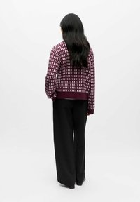 Stickad tröja i djup mörkröd med ett geometriskt vitt mönster, med avslappnad passform och ribbad fåll, kombinerad med vida svarta byxor.