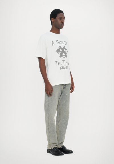 White oversized graphic t-shirt with black print, gray denim jeans, and black shoes. The shirt features a design with geometric shapes and text.