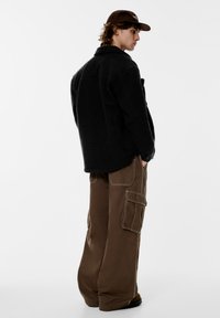 Sort fleecejakke med krave, kombineret med løstsiddende brune cargobukser med flere lommer og kontrastsyninger.
