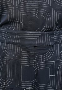 Black fabric with white geometric stitching in a repetitive pattern, featuring a waistband and pleats for design detail.