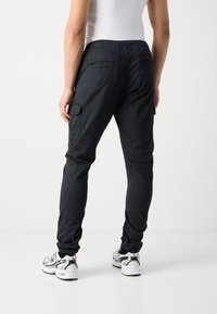 Zwarte cargobroek met een elastische tailleband, zijzakken en taps toelopende boorden. Gemaakt van een lichte stof met een gladde textuur.