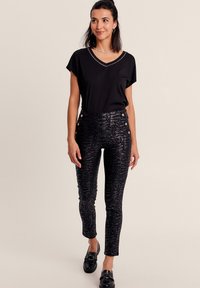 T-shirt nera con scollo a V e maniche corte, abbinata a pantaloni neri a vita alta con pattern, dotati di bottoni laterali e una vestibilità slim.