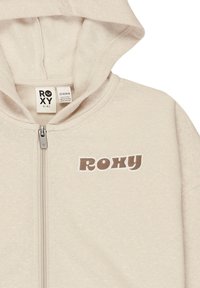 Svetlo béžová mikina na zips s kapucňou, s hnedým logom "ROXY" vytlačeným na ľavej strane. Mäkká, štruktúrovaná tkanina a štandardné manžety.