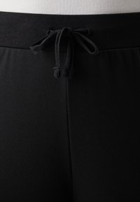 Ceinture élastique noire avec cordon de serrage réglable ; tissu doux et lisse ; design ajusté ; sans logos ni motifs visibles.