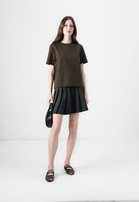 Dark brown short-sleeve t-shirt paired with a pleated black skirt. Accessories include a small black handbag and leopard print shoes.