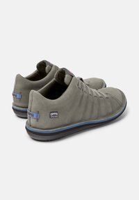 Scarpe Camper grigie dal design elegante, con un accento blu lungo la suola e un'etichetta nera sul tallone, visibili da una prospettiva angolata.