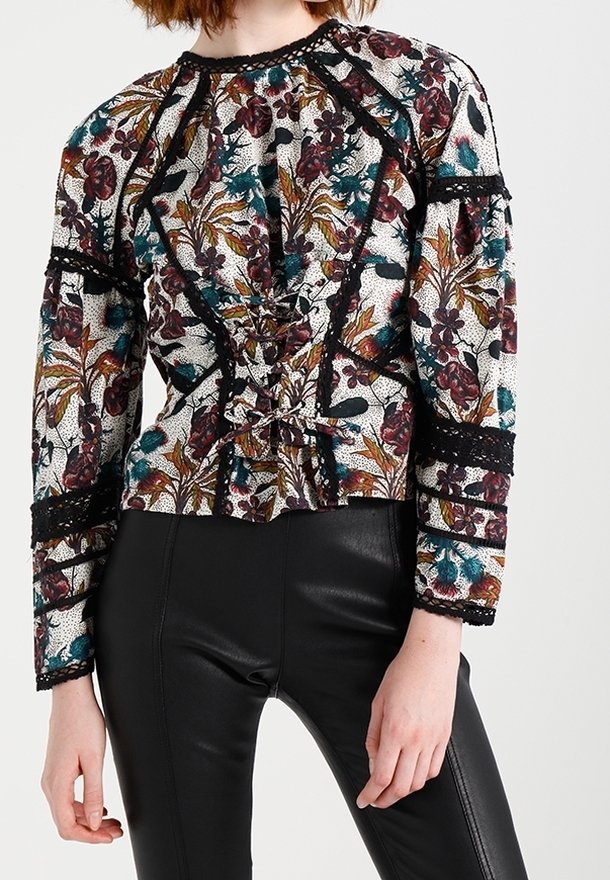 Kukkakuosisesti valkoinen pusero, jossa on monivärisiä kuvioita, pitkät hihat, kokoontuva etuosa ja mustat pitsiyksityiskohdat. Yhdistetty mustiin sukkahousuihin.