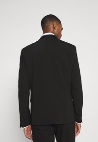 Sacou negru cu un design structurat, rever cu decupaj, și două butoane, fabricat dintr-un material fin și cu o croială ajustată.