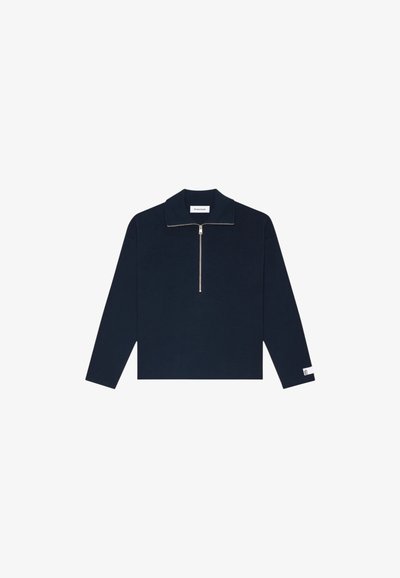 Pull-over long à manches en marine avec un col zippé, texture côtelée et petite étiquette logo sur la manche. Présente une coupe droite et décontractée.