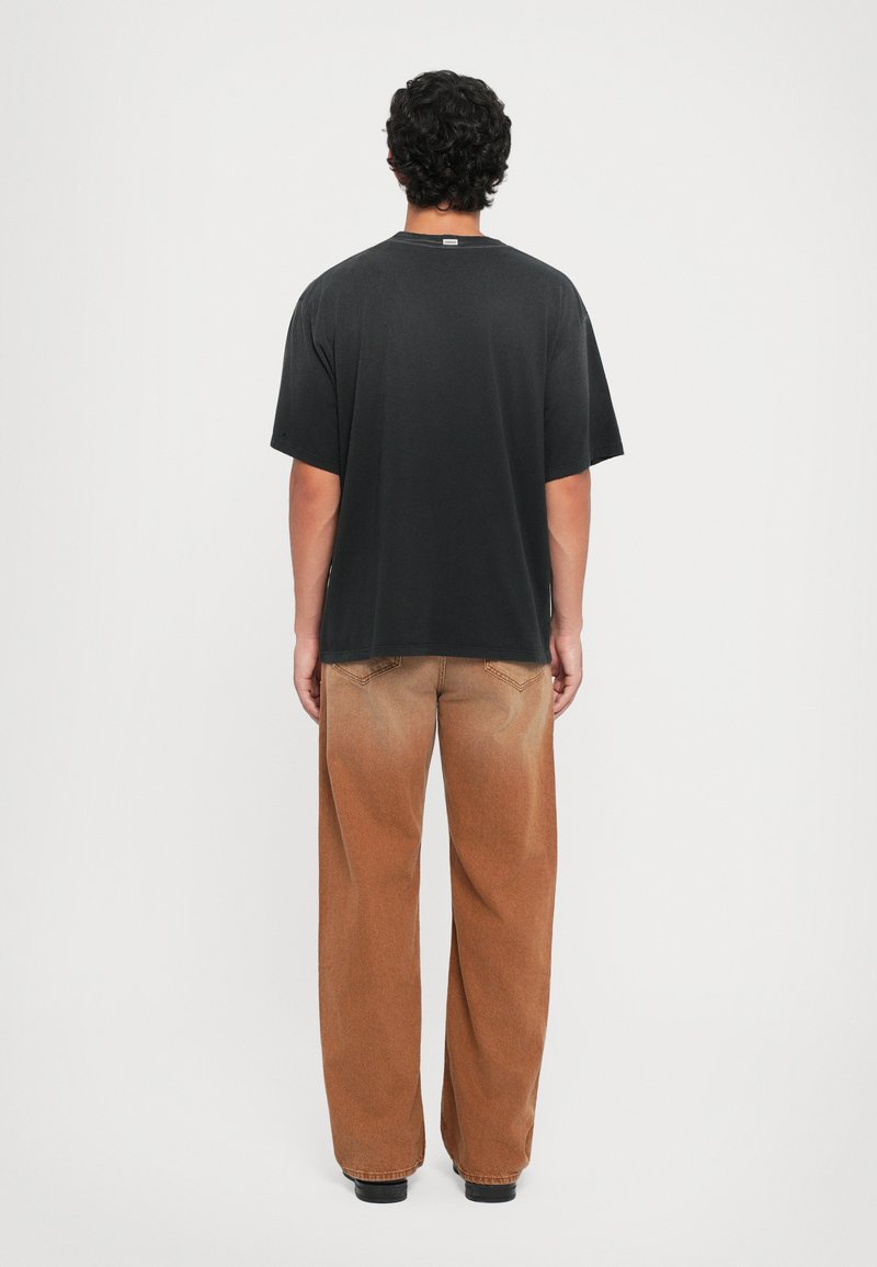 Black cotton oversized t-shirt with short sleeves, paired with brown wide-leg pants featuring subtle fading and standard back pockets.
