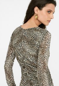 Top fitted cu mânecă lungă, într-un model de imprimeu leopard bej și maro, având o textură strânsă pe părțile laterale și un decolteu rotund.