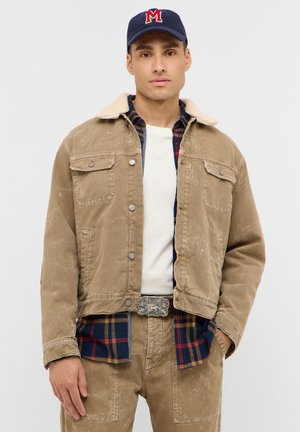 Tan corduroy jacket with a beige shearling collar, paired with a plaid shirt. Features front pockets and a silver belt buckle.