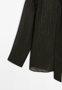 Czarna koszula z pionowymi złotymi metalicznymi paskami, długimi rękawami z mankietami na guziki oraz miękką, teksturowaną tkaniną.