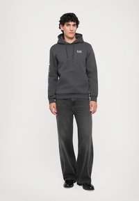 Gray hoodie with front pocket, drawstrings, and logo. Paired with dark wide-leg jeans and black shoes. Simple and functional design.