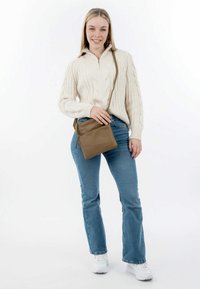 Borsa a tracolla sintetica marrone con una texture liscia e scomparti con zip, indossata sopra un maglione beige a trecce e jeans svasati blu.