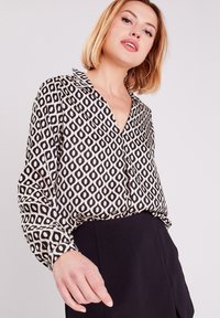 Blouse à motifs avec un design géométrique noir et crème, dotée d'un col, d'une fermeture à boutons sur le devant et de manches longues. Basique en noir.