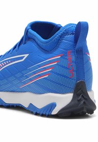 Blauer Sportschuh mit strukturiertem Obermaterial, roten und weißen Akzenten, einem flachen Design und einer Gummisohle mit multidirektionalen Stollen.