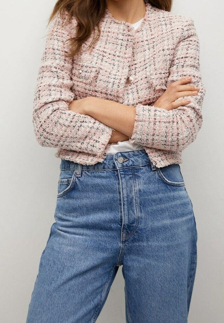 Rosa Tweedjacke mit strukturiertem Stoff, vorne mit Knopfverschluss und dreiviertellangen Ärmeln, kombiniert mit hoch taillierten blauen Jeans.