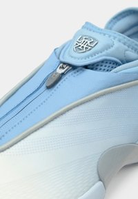 Αθλητικό παπούτσι ανοιχτού μπλε χρώματος με υφασμένη επιφάνεια, κλείσιμο με φερμουάρ και ασημένιες λεπτομέρειες λογότυπου· διαθέτει λείο, στρογγυλεμένο μύτη και γκρι λεπτομέρειες.