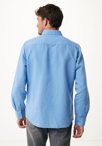 Světle modrá košile s dlouhými rukávy, s límečkem na knoflíky, zadním skladem a knoflíky na manžetách. Vyrobena z měkké, texturované látky.