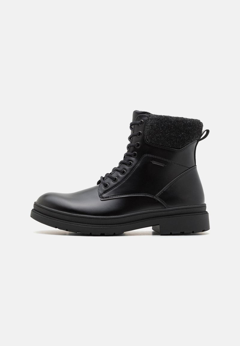 Bota de cuero negro hasta el tobillo con un collar de tela negra texturizada, punta redonda y cierre de cordones. Cuenta con una suela de goma resistente y una lengüeta.