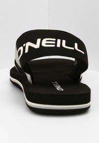 Mustat flip-flopit, joissa on leveä kangashihna, jossa on valkoinen "O'NEILL"-logo, teksturoitu pohja ja hieno valkoinen yksityiskohta reunassa.